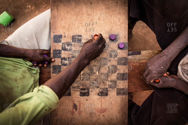 Two men playing checkers on a hand-painted board and bottlecaps