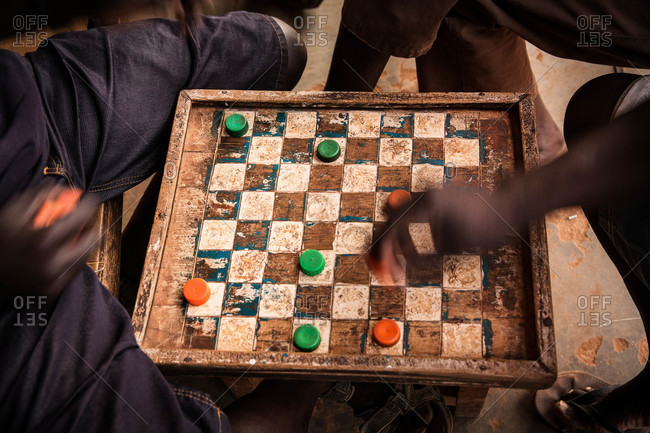 Men playing a game of checkers on a worn board with bottlecaps