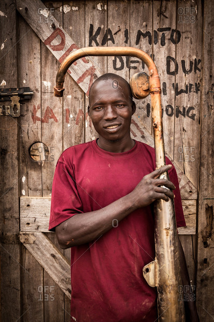 Paicho, Uganda - March 5, 2015: Young man standing in a workshop doorway with a water pipe
