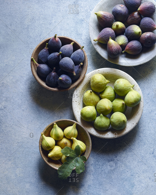 Overhead of four bowls of fresh purple and green figs