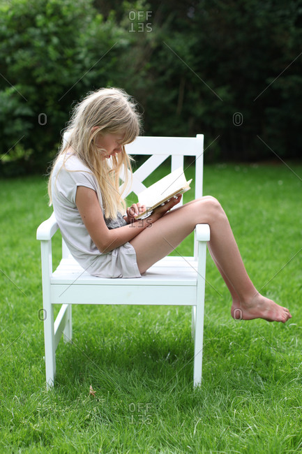 Teenage girl sitting sideways in white garden chair on green lawn