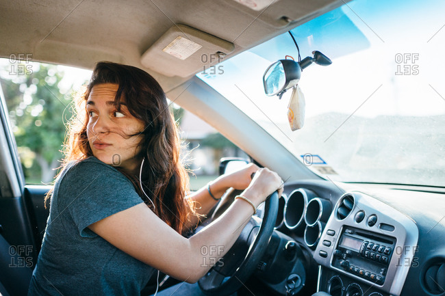Teenage girl behind the wheel looks behind her as she's driving