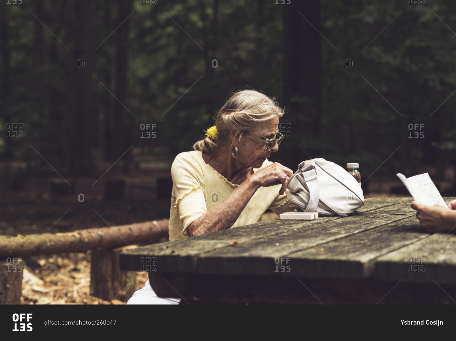 Senior woman at a picnic table looking through handbag