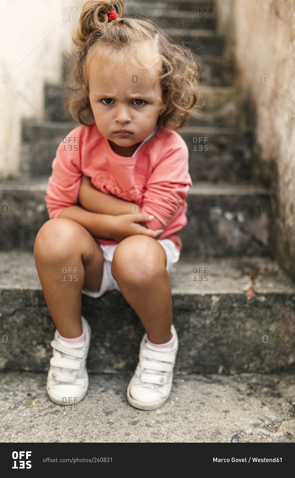 Portrait of little girl sitting on steps pouting mouth