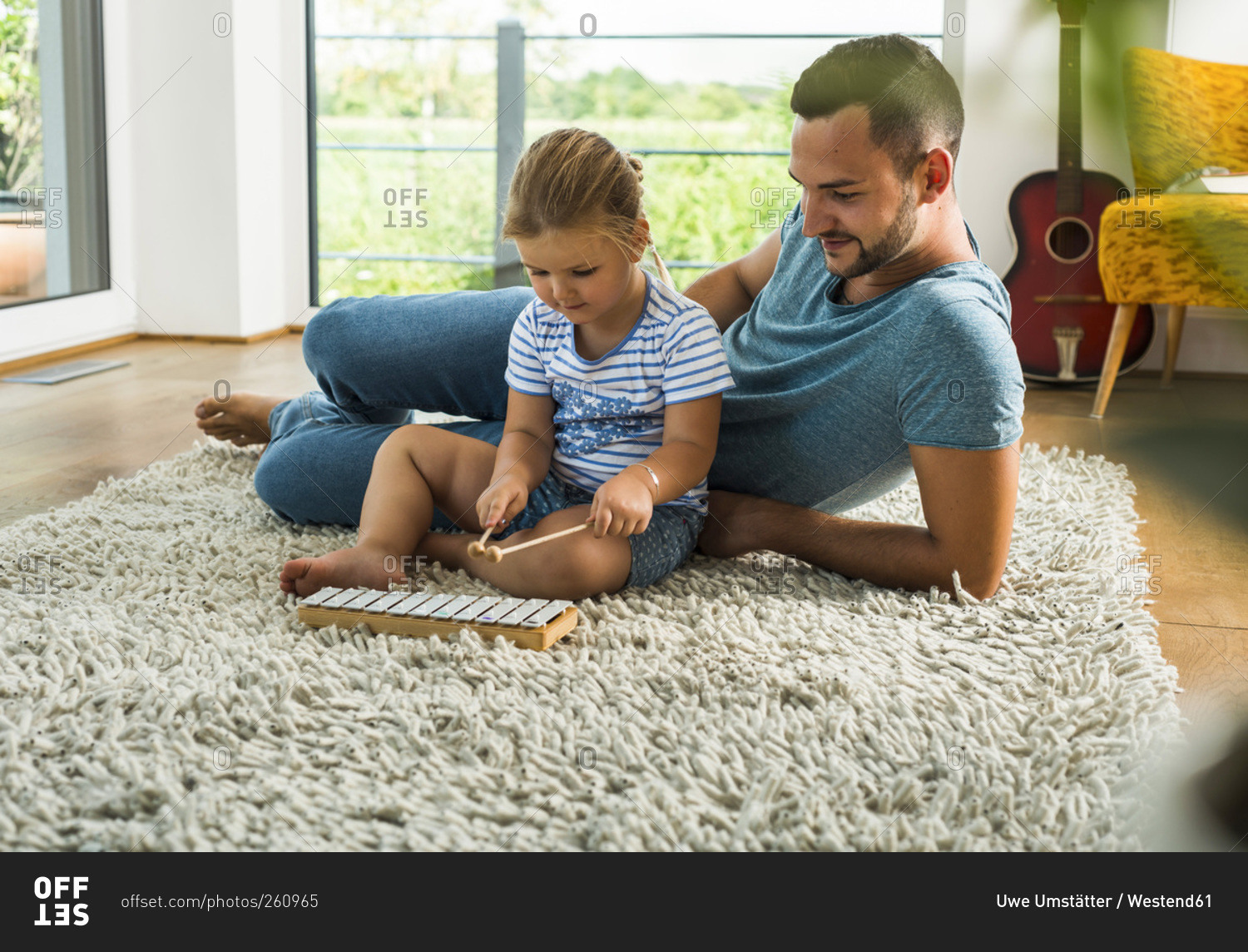 Father with daughter on rug playing glockenspiel