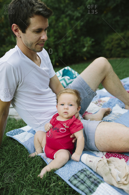 A newborn baby leans against her dad at a family picnic
