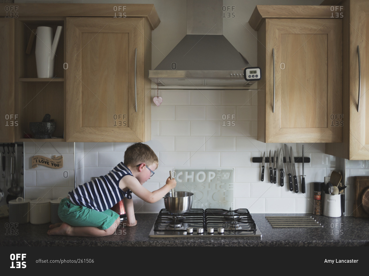 Young boy kneeling on counter stirring a pot on stove