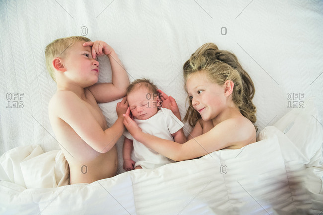 Siblings cuddle their newborn sibling in bed