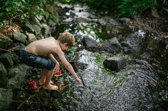 Shirtless Young Boy Crouches While Pointing A Stick In Creek St