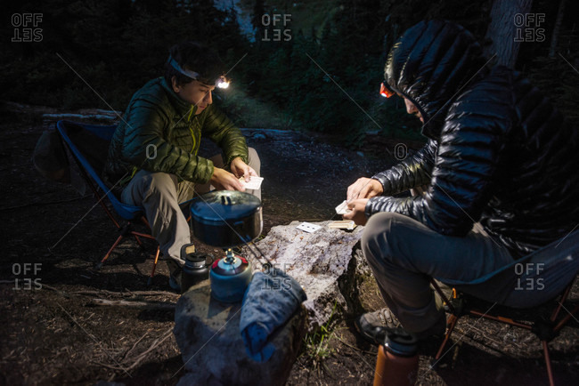 Father and son playing cards by flashlight while camping