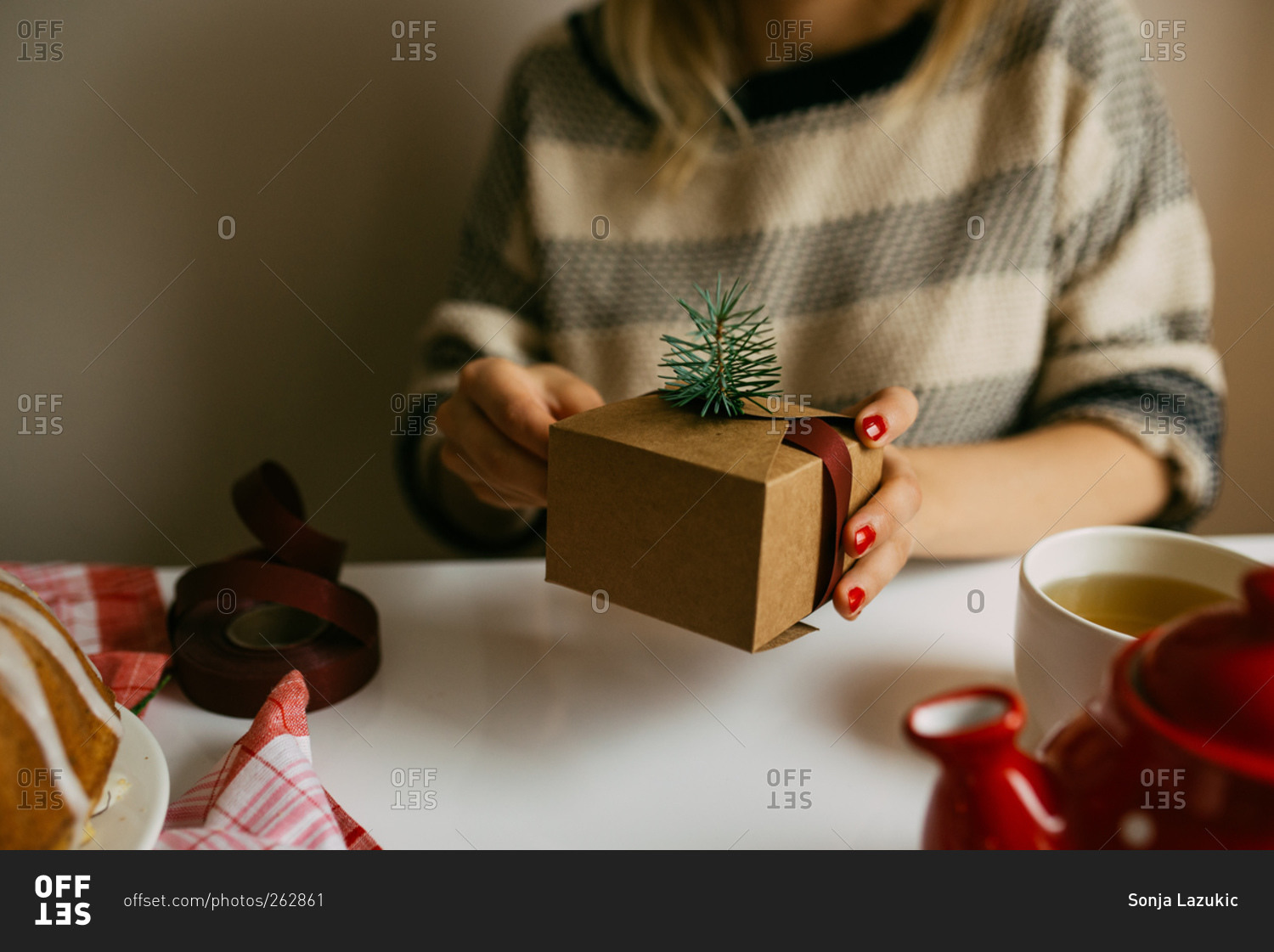 Woman wrapping gift box with pine and ribbon