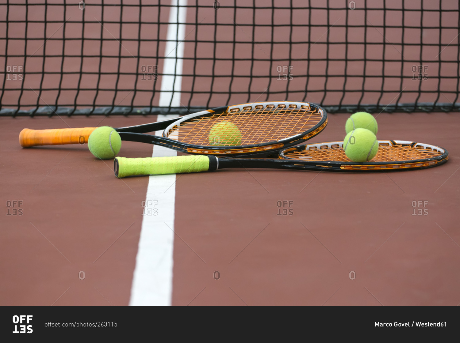 Two tennis rackets and four balls lying on ground of tennis court