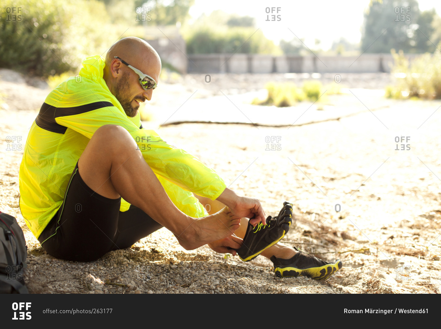 Man in sports wear sitting on ground putting his shoes on