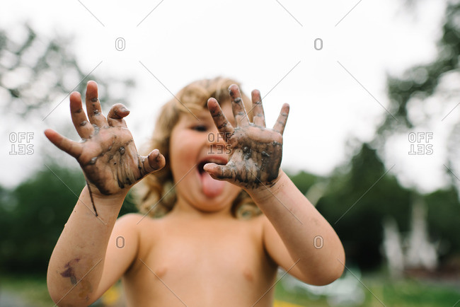 Little girl holding up mud covered hands