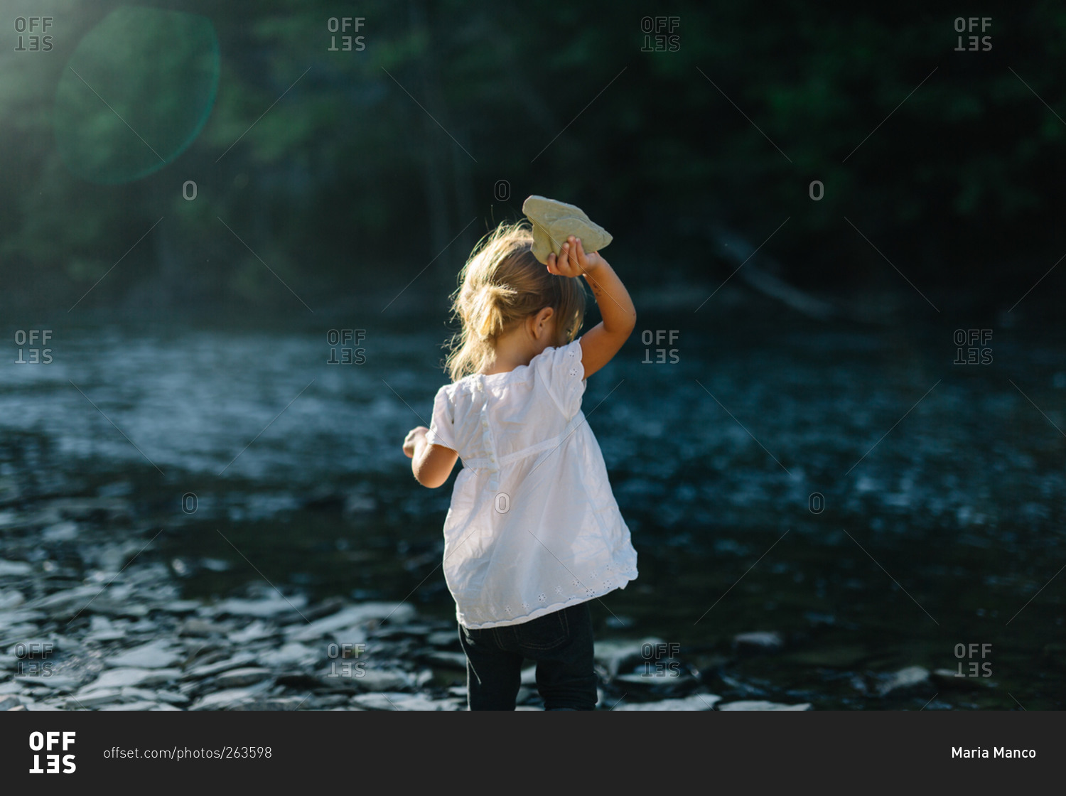 Girl throwing a large rock into a river stock photo - OFFSET