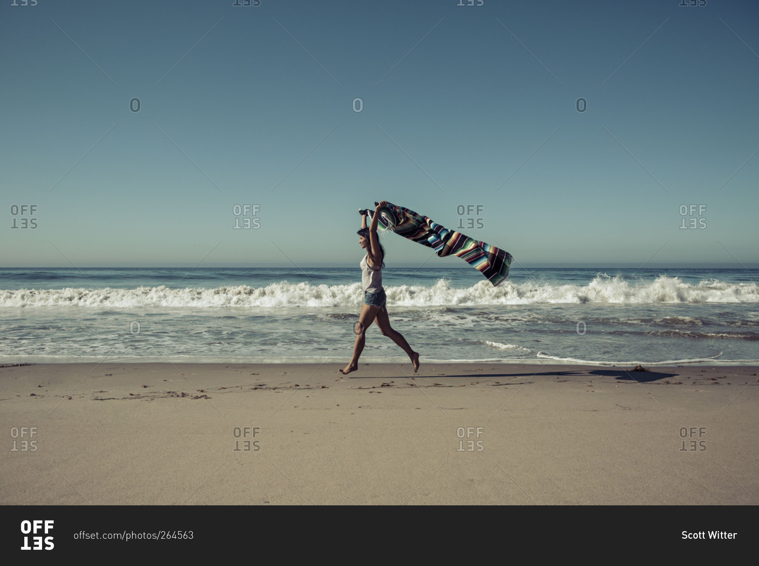 Woman jogging with a multicolored blanket on a beach stock photo OFFSET