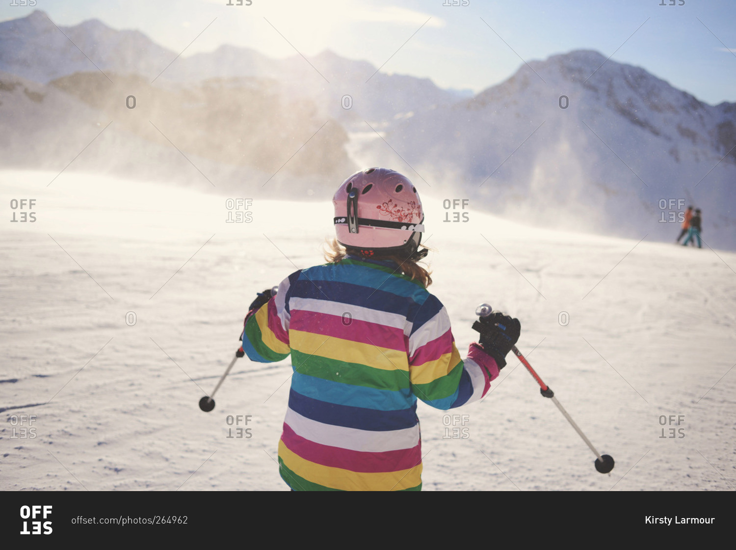 Girl in striped jacket and pink helmet skiing down slope