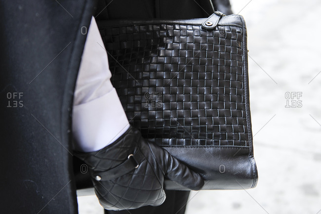 A woman in quilted gloves carries a woven handbag