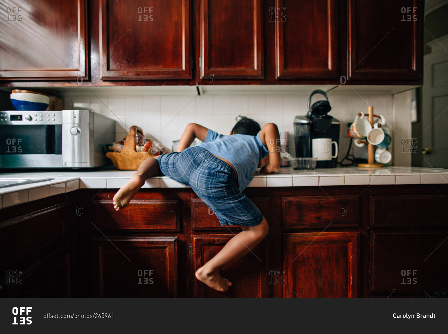 Boy climbing onto a kitchen counter stock photo OFFSET