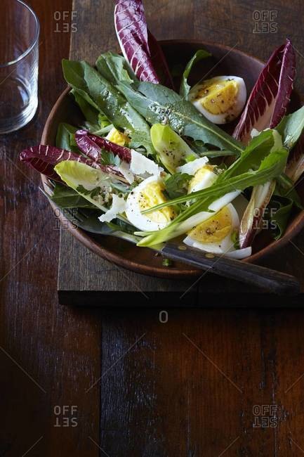 Leafy green salad with boiled egg and parmesan in a wood bowl, studio shot on dark, wooden background