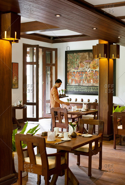 Siem Reap, Cambodia - February 24, 2009: Young Asian server sets up tables in dining room of luxury resort in Siem Reap, Cambodia