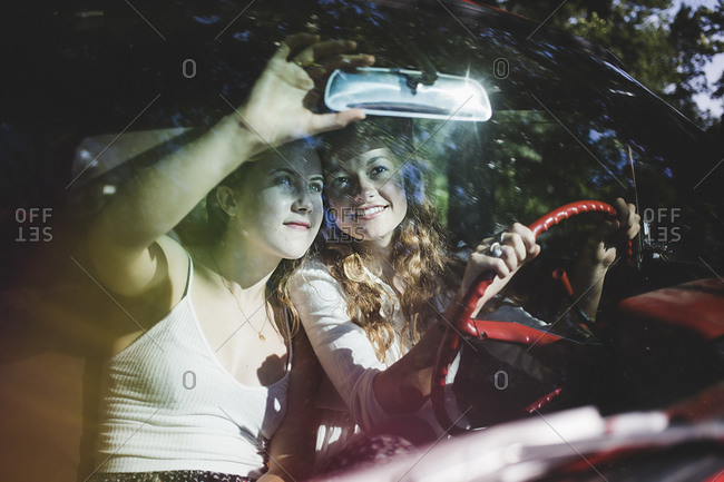 Two women look at themselves in a rear view mirror of a car
