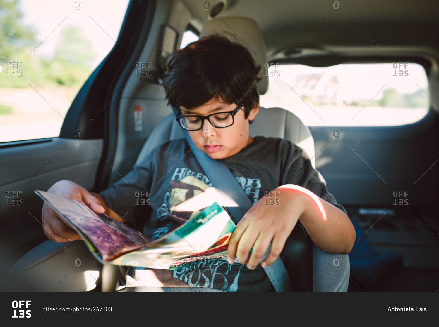 A boy reads a magazine in the back of a minivan
