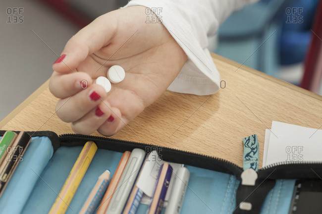 Little girl holding medicine at her school desk