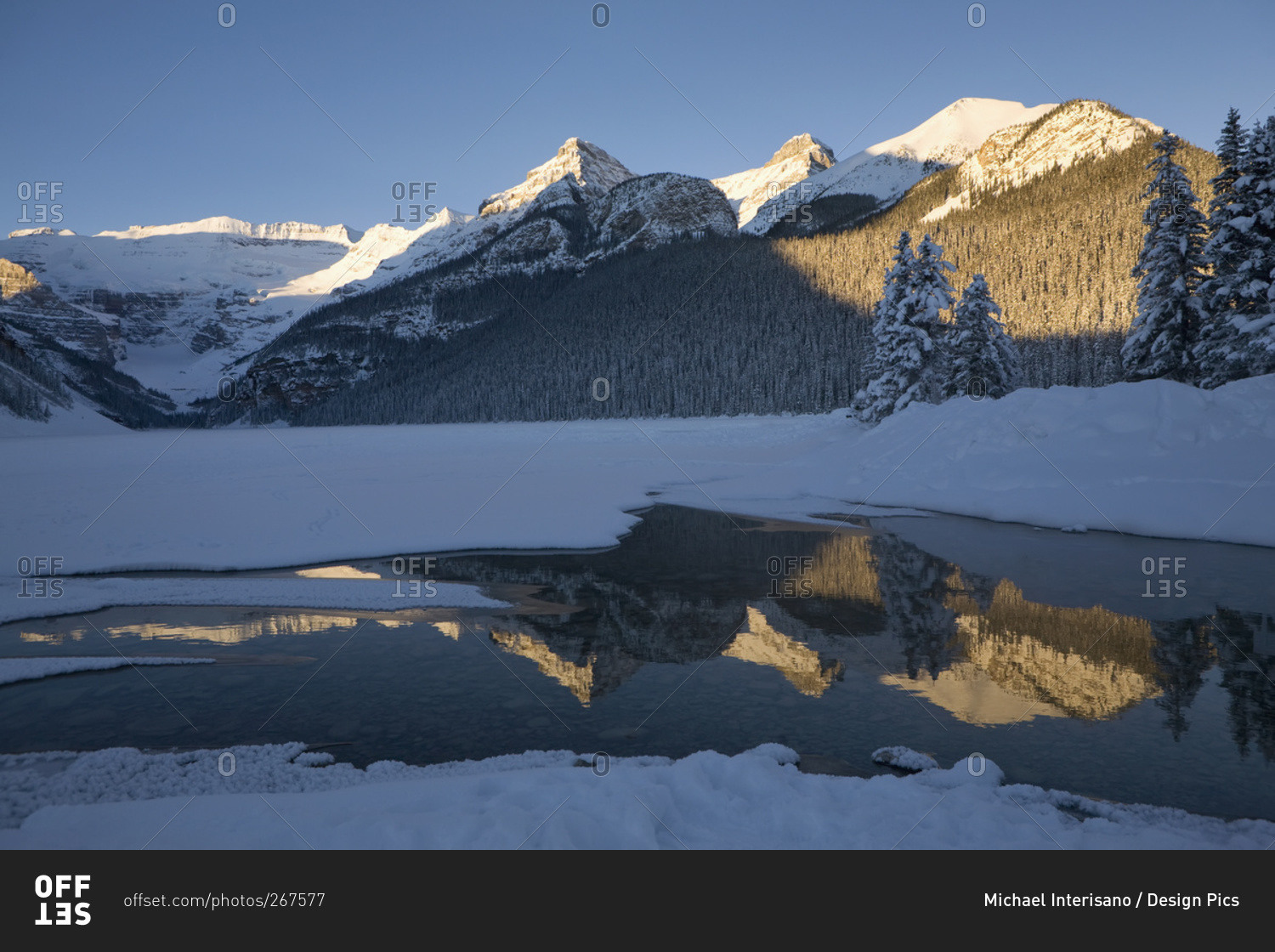 Early morning sunlit snow covered mountains reflecting in a lake with deep blue sky, Lake Louise, Alberta, Canada