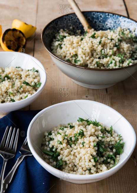Serving dish and two bowls of Israeli couscous and grilled lemon