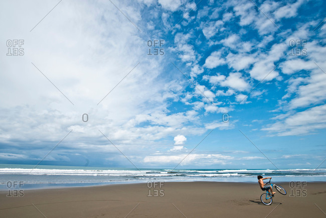 A Costa Rican boy rides his bike on a desolate beach on a sunny day