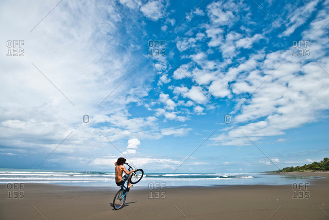 A Costa Rican boy rides his bike on a desolate beach