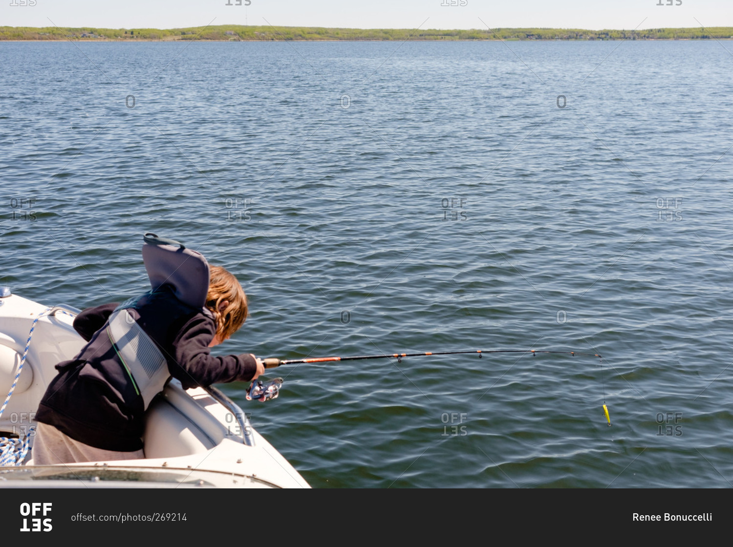 Boy fishing in boat looking overboard stock photo - OFFSET