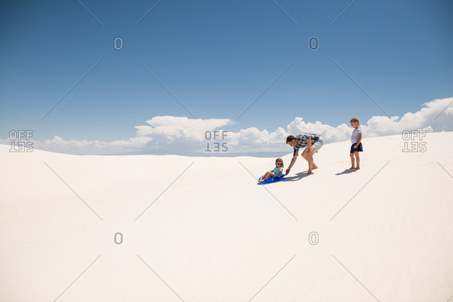 Father pushing his daughter in a sled on a white sand dune, White Sands National Monument in Alamogordo, New Mexico