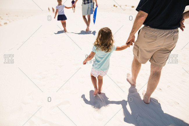 Little girl and grandfather holding hands as they walk across white sand dunes, White Sands National Monument in Alamogordo, New Mexico