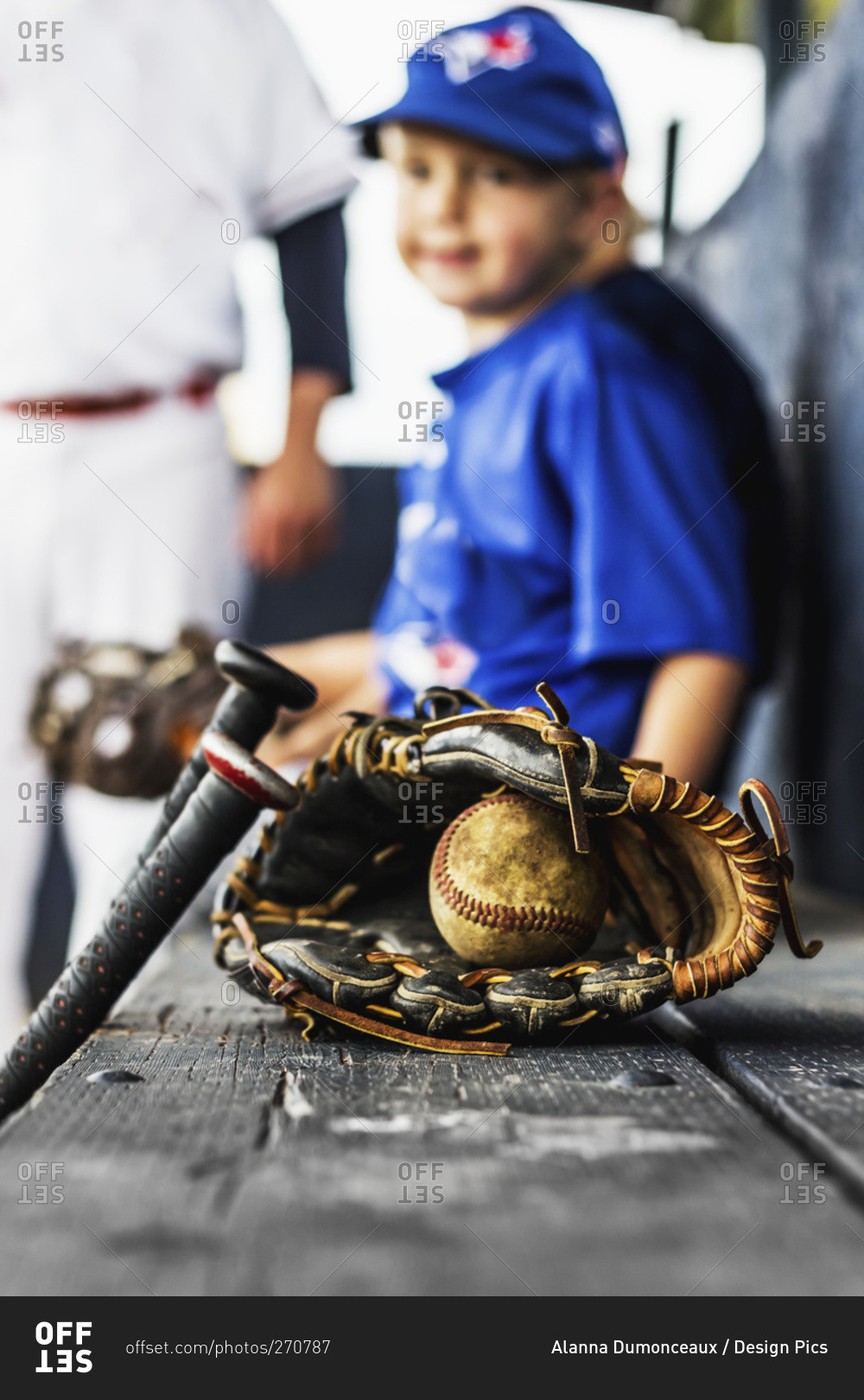 Two ball players in uniform sit in the dugout with their glove and baseball in focus in the foreground, Fort McMurray, Alberta, Canada
