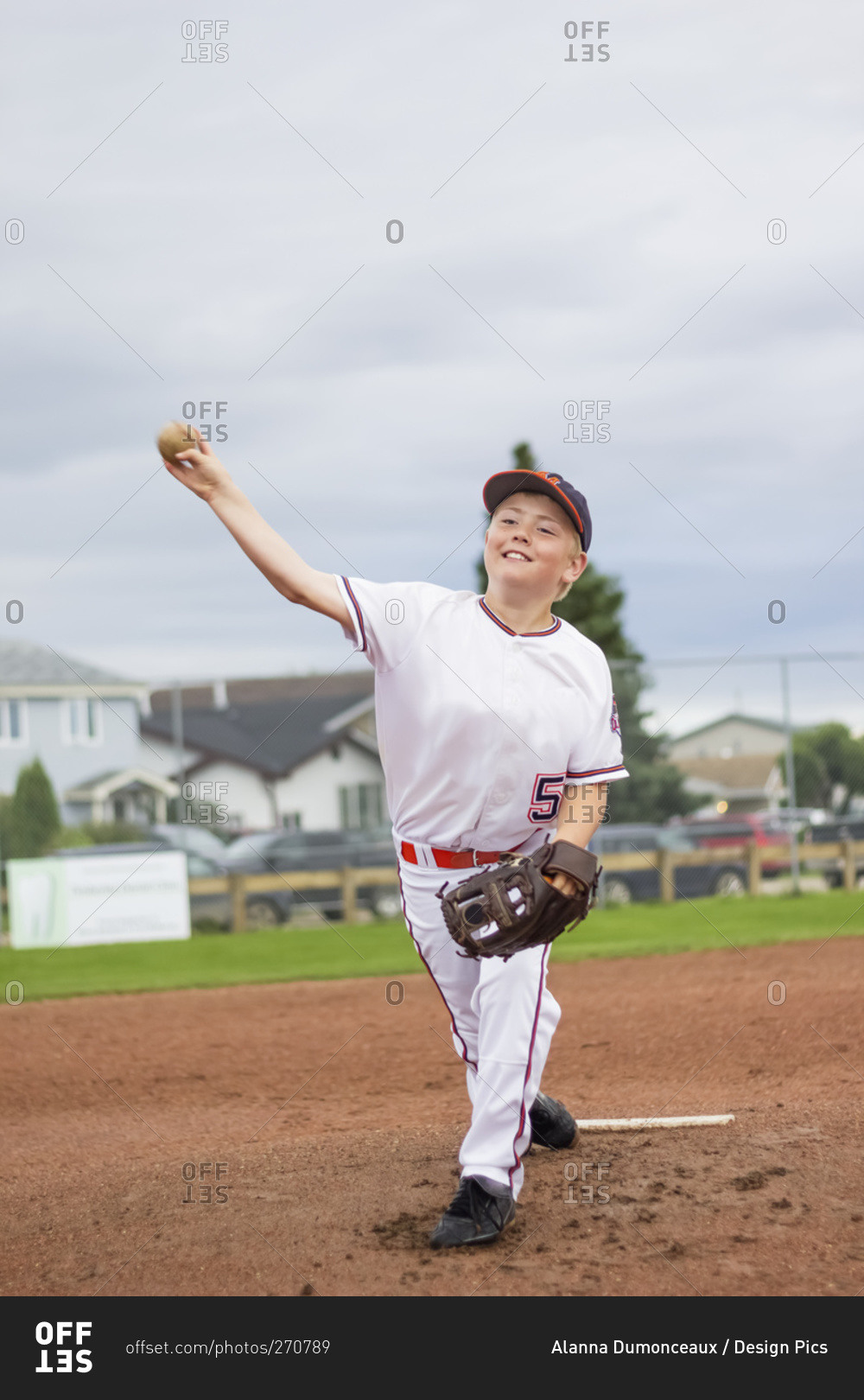 A young boy pitches the baseball from the pitchers mound during a ball game in a white uniform with a baseball and glove, Fort McMurray, Alberta, Canada