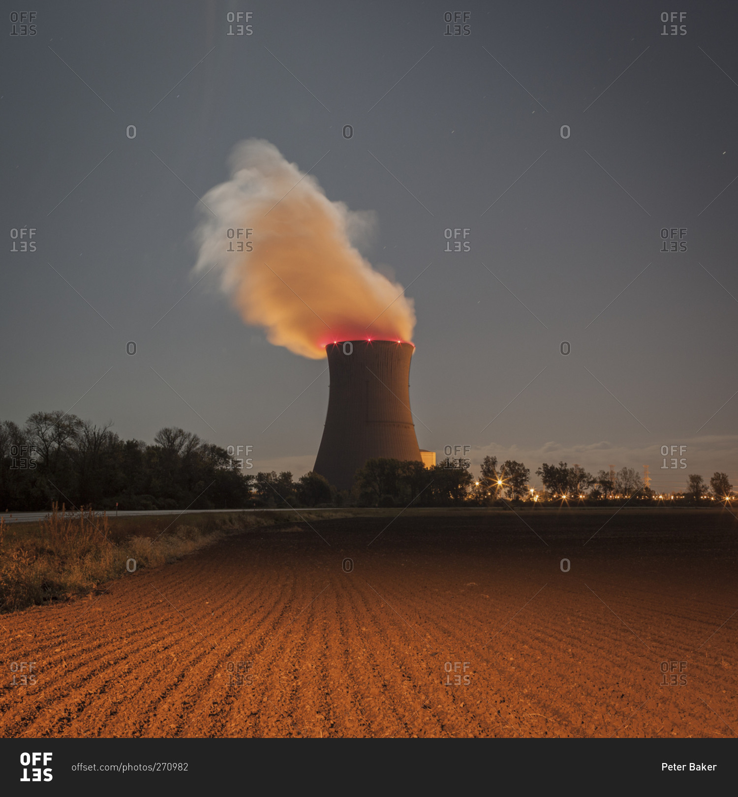 Cooling tower at a nuclear power plant next to a farm field at dusk