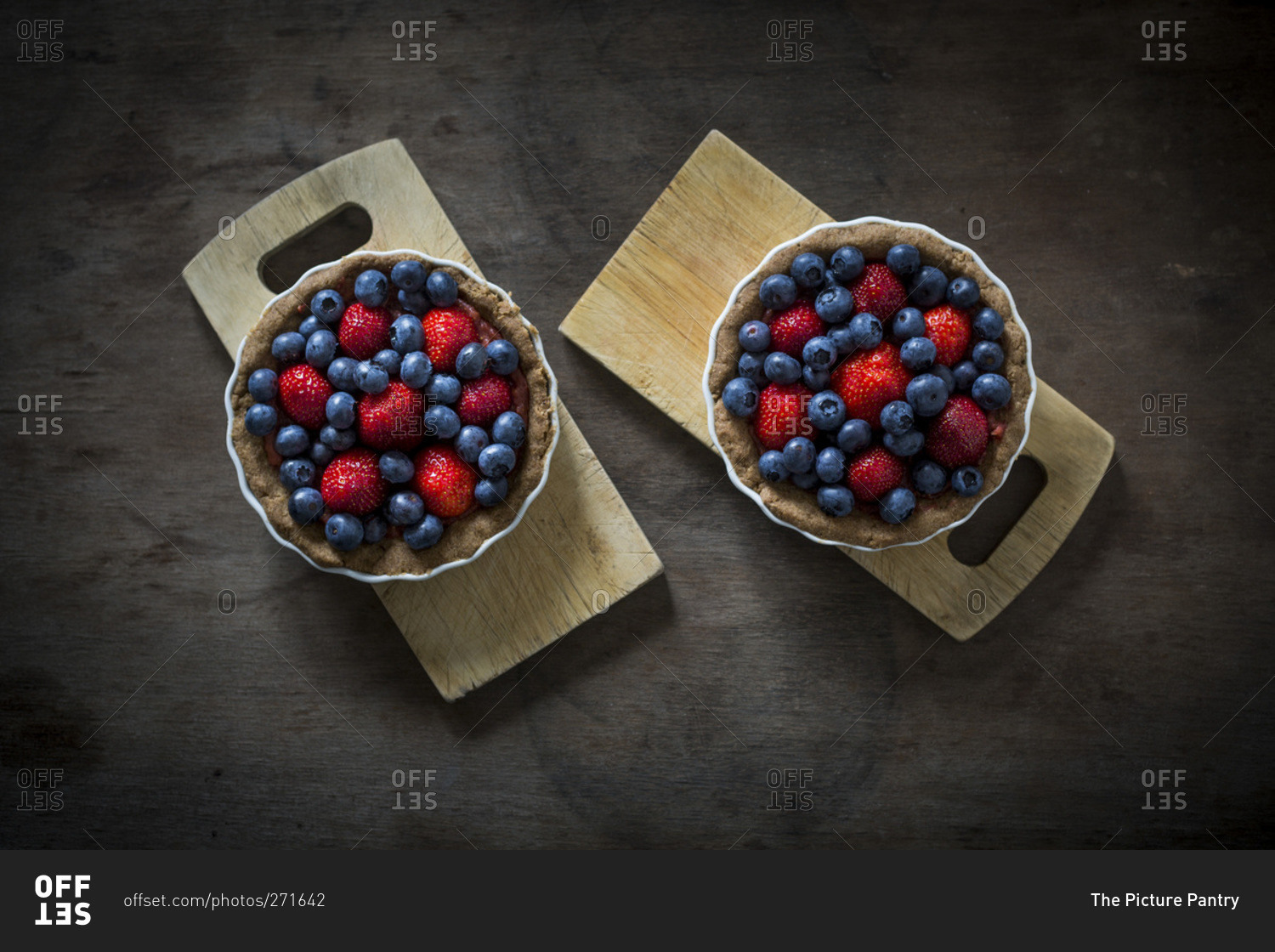 Berry tartlets in baking dishes on wooden boards