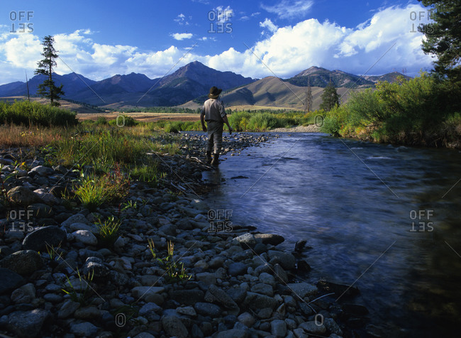 Man standing at the edge of a creek looking at distant mountains