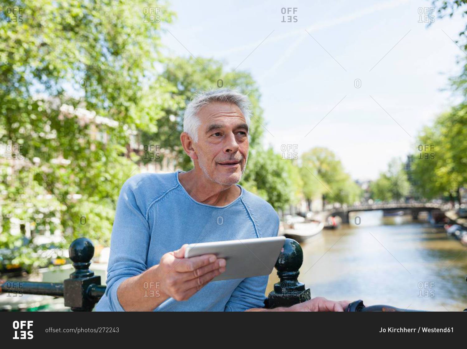 Senior man with digital tablet at town canal