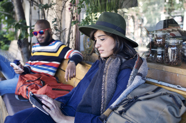 Young couple sitting on an outdoor bench checking their phones
