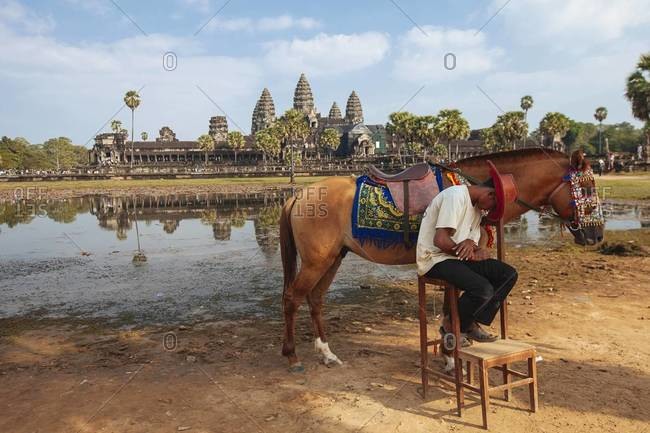 Siem Reap, Cambodia - December 28, 2013: A Cambodian man taking a nap next to his horse in the Angkor Wat Temple