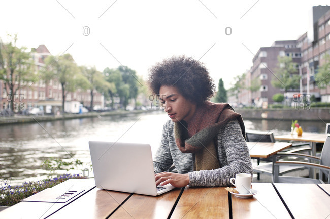 Man using laptop at outdoor cafe along the canal in Amsterdam