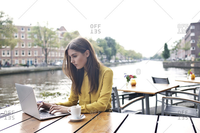 Woman using laptop at outdoor cafe along the canal in Amsterdam