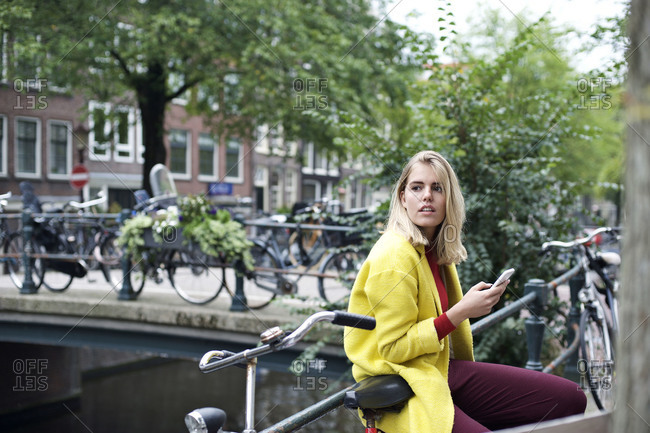Woman leaning against railing on bridge in Amsterdam and using her smartphone