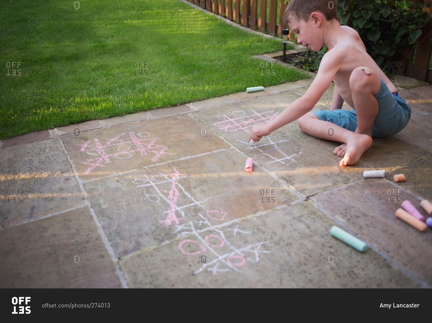 Boy drawing tic tac toe boards on sidewalk with chalk