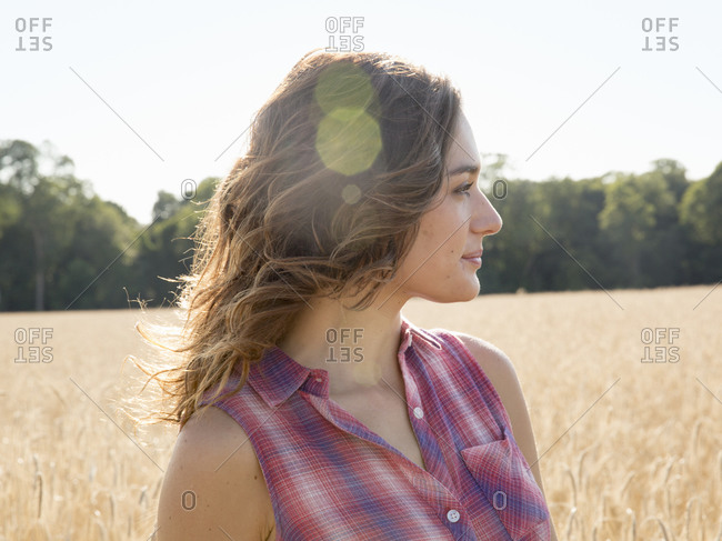 Profile of a young woman standing in a field of tall ripe wheat