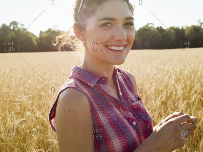 Smiling young woman wearing a checkered shirt standing in a wheat field