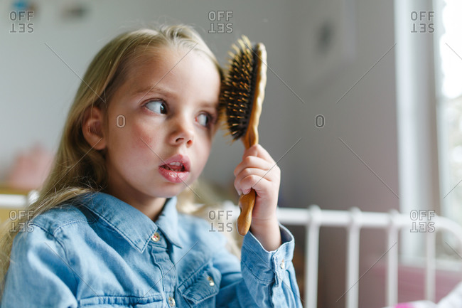 Portrait of girl on bed brushing her hair stock photo - OFFSET